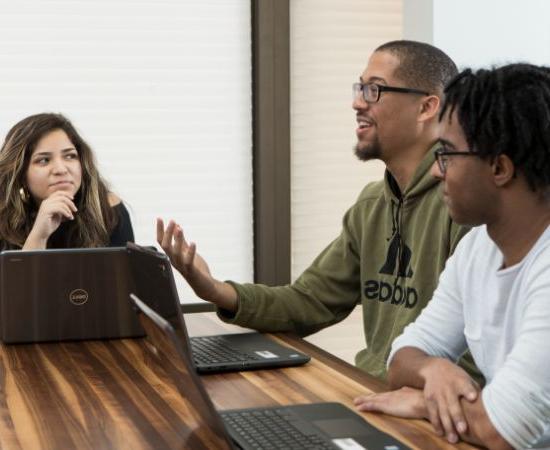 Students talking at a table with laptops